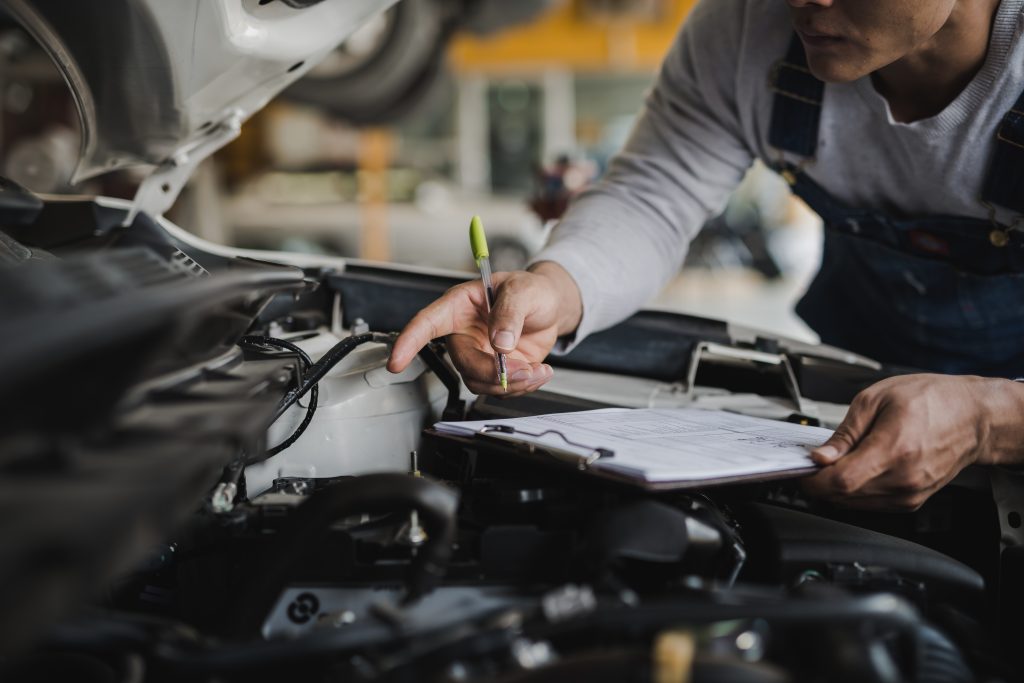 A mechanic inspecting a car engine with a clipboard.
