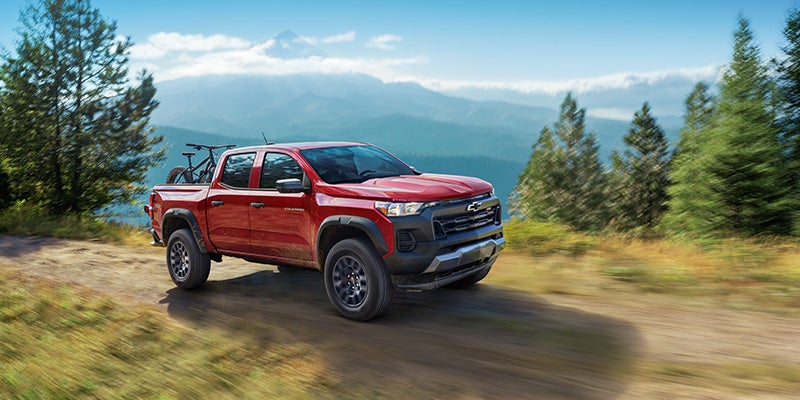 Red Chevrolet Colorado pickup truck driving on a mountain trail with scenic forest views